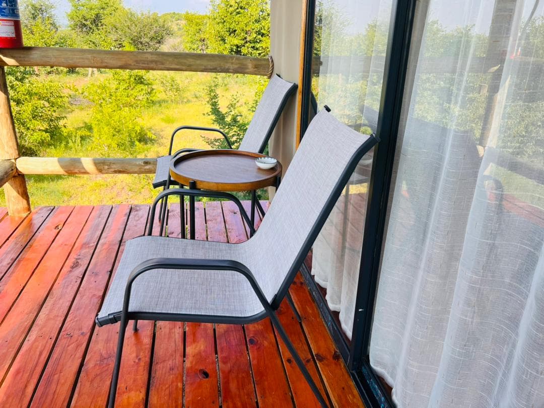 Two chairs and a small table on the private balcony of a chalet, looking out into green bush