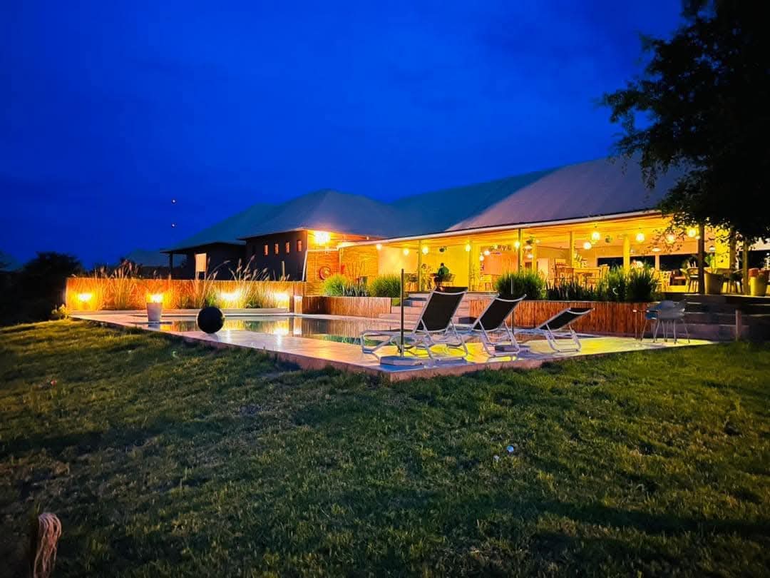 Xhabe Safari Lodge at dusk, the main building glowing warm behind the lit pool